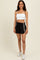woman wearing a white cropped tank top and black athletic shorts with white side stripes, standing and smiling