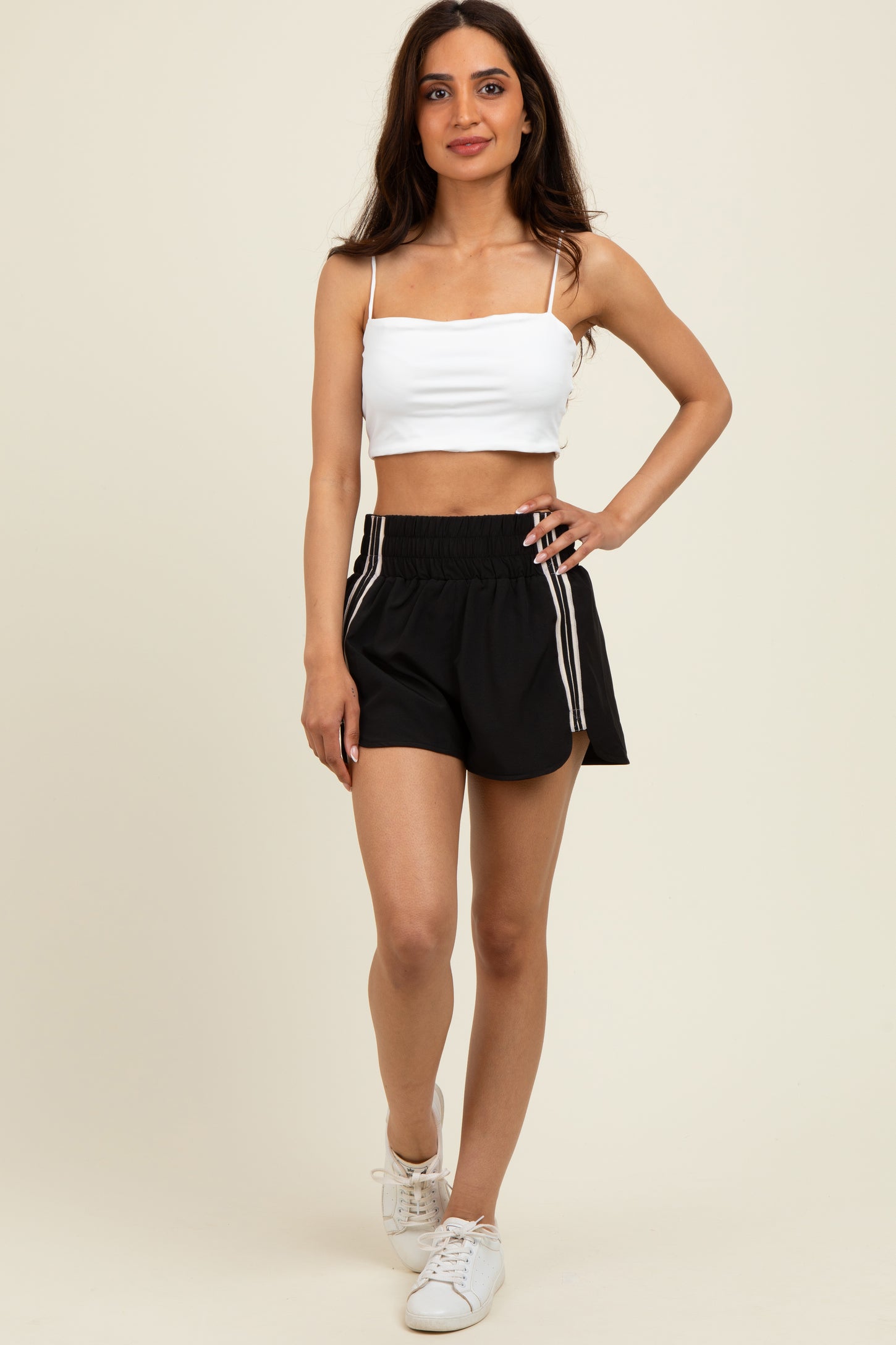 woman wearing a white cropped tank top and black athletic shorts with side stripes and white sneakers