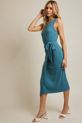 woman wearing a teal sleeveless midi dress with a tie waist and side slit, standing elegantly