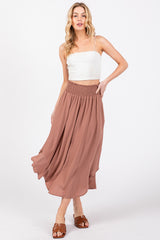 woman wearing a mauve smocked waist maxi skirt and a white crop top, posing with one hand on her hip