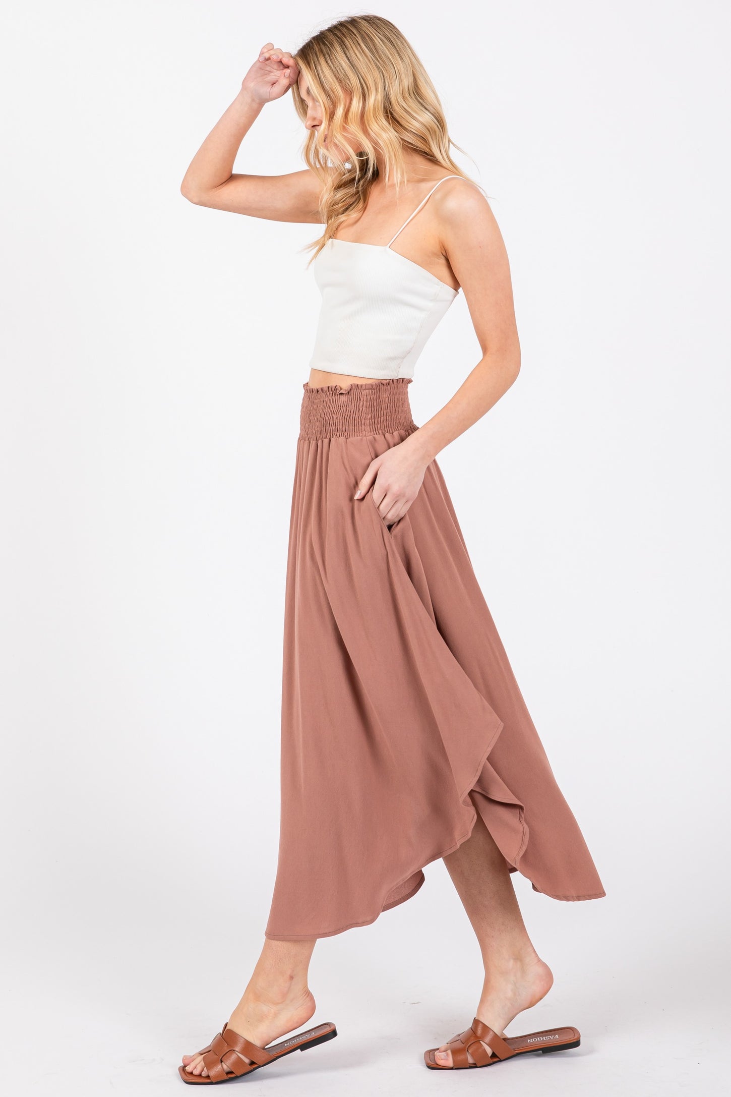 woman wearing a white crop top and a long dusty rose skirt with a smocked waist, walking sideways
