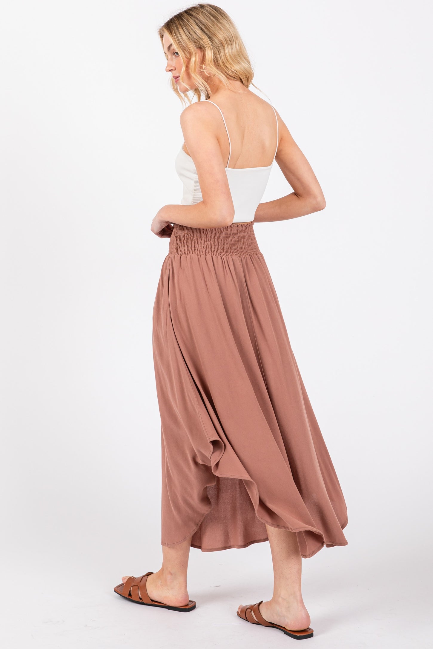 woman wearing a white spaghetti strap top and a flowy dusty rose maxi skirt with a smocked waistband
