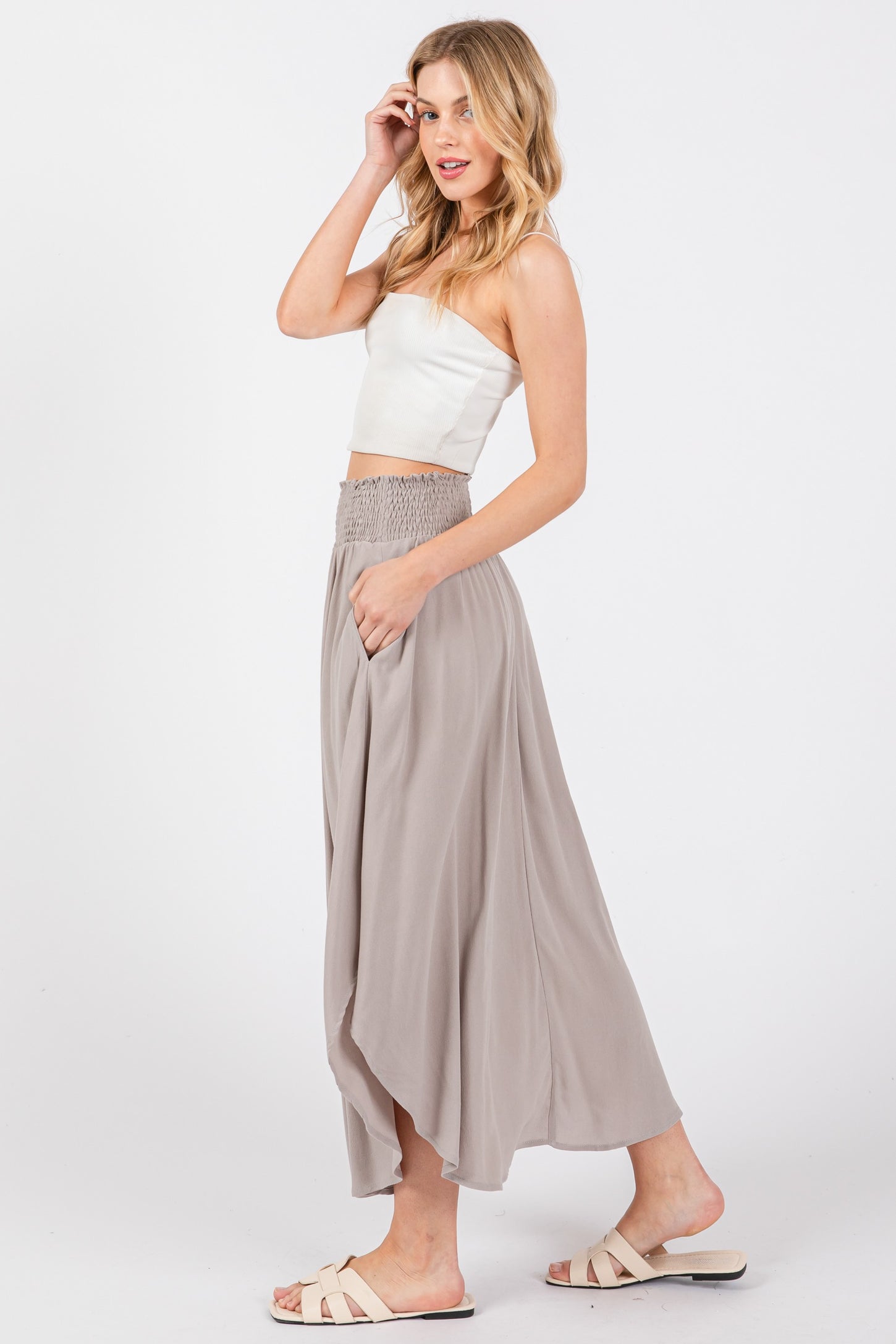 woman wearing a white fitted crop top and a flowy light gray maxi skirt with a smocked waistband