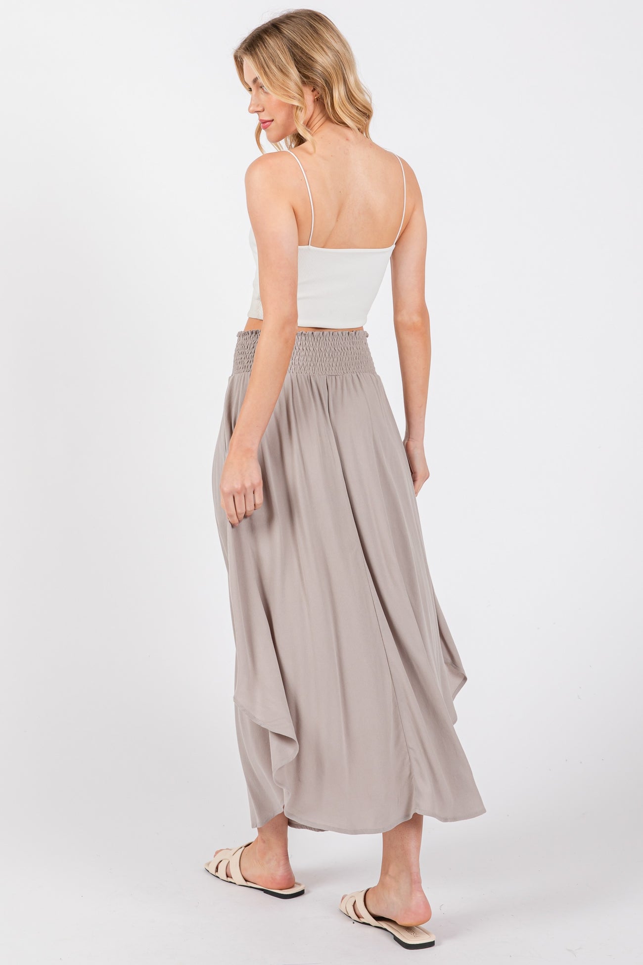 woman wearing a light grey maxi skirt with a smocked waistband and a white spaghetti strap top, viewed from the back
