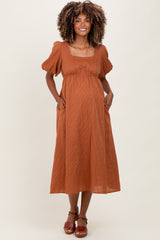 woman wearing a rust-colored maternity midi dress with short puff sleeves and pockets, showcasing her baby bump