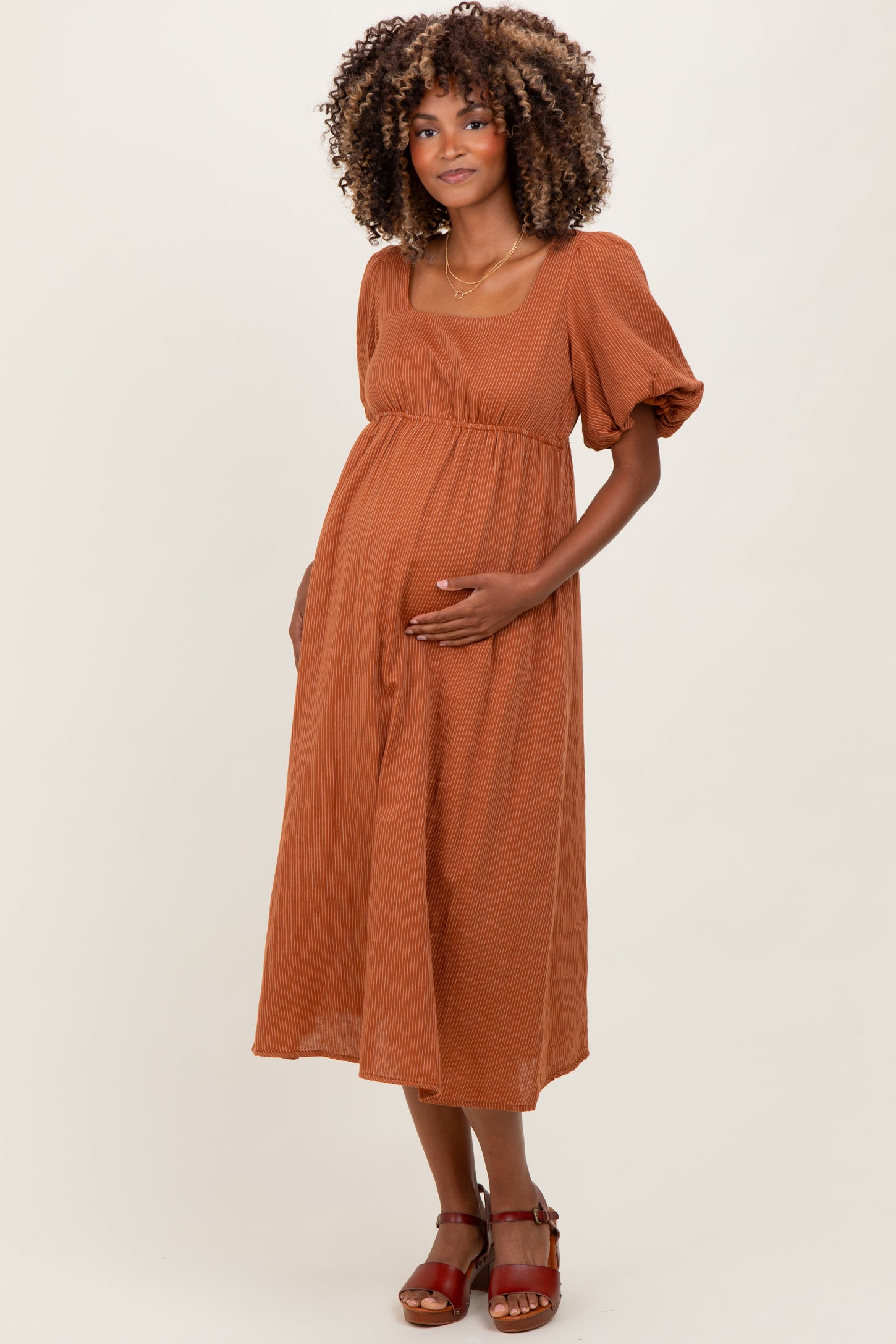 woman wearing a rust-colored maternity dress with puff sleeves and holding her baby bump