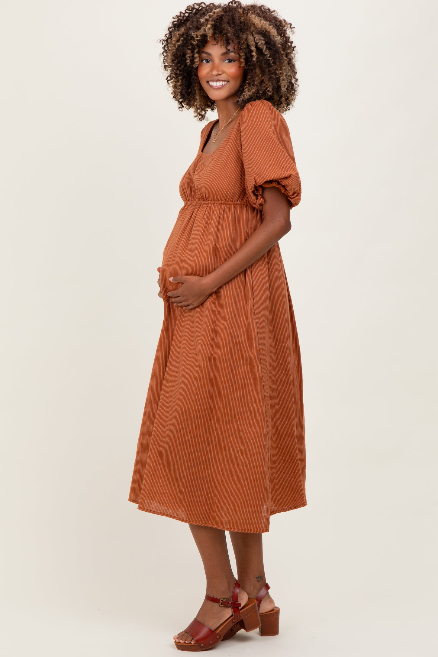 woman wearing a rust colored maternity dress with short puff sleeves and a fitted bodice, gently cradling her baby bump