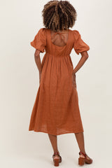 woman wearing a rust-colored maternity dress with puff sleeves and an open back detail, standing in profile