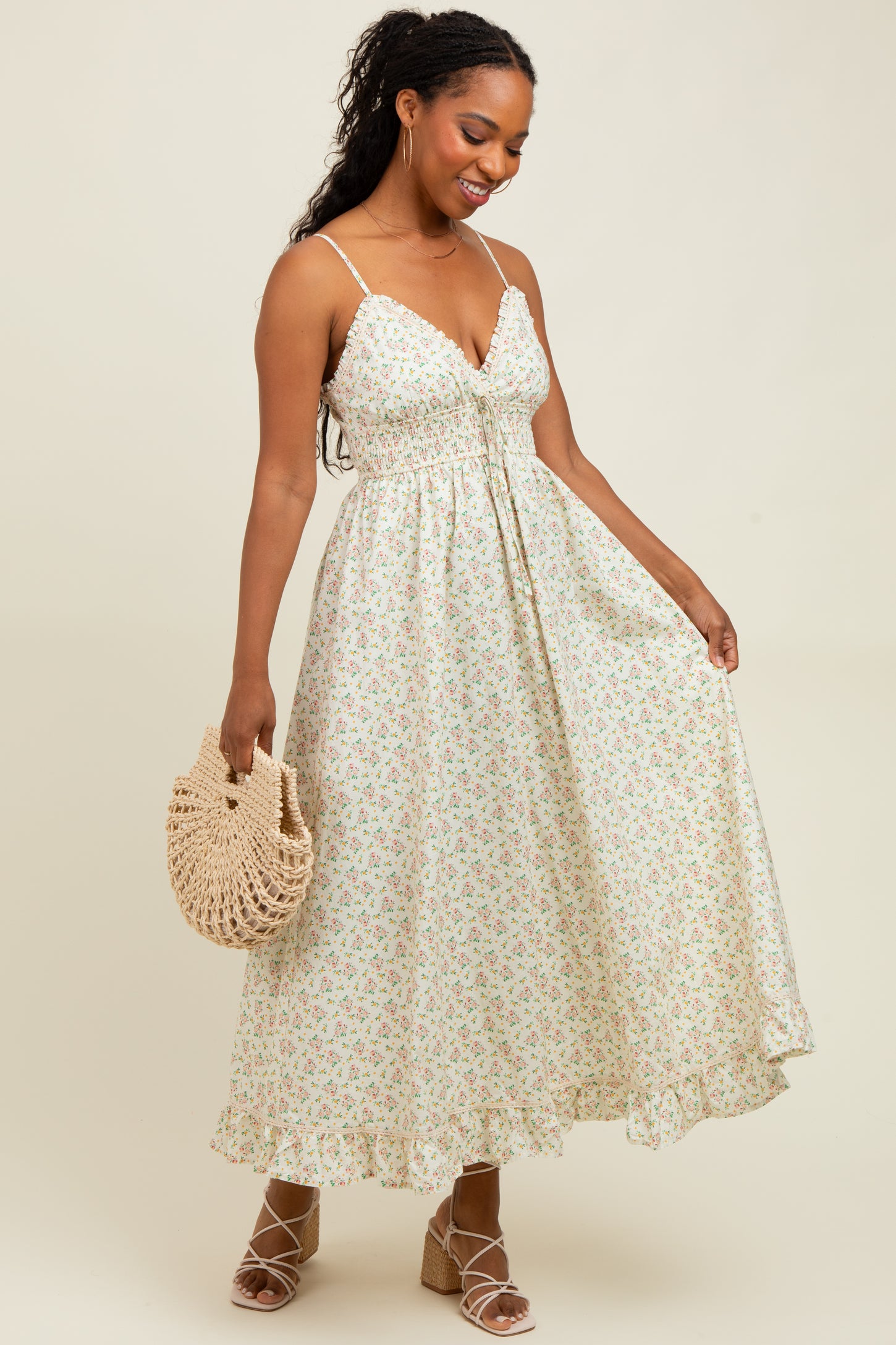 woman wearing a floral maxi dress with adjustable straps, holding a woven bag and standing against a light background