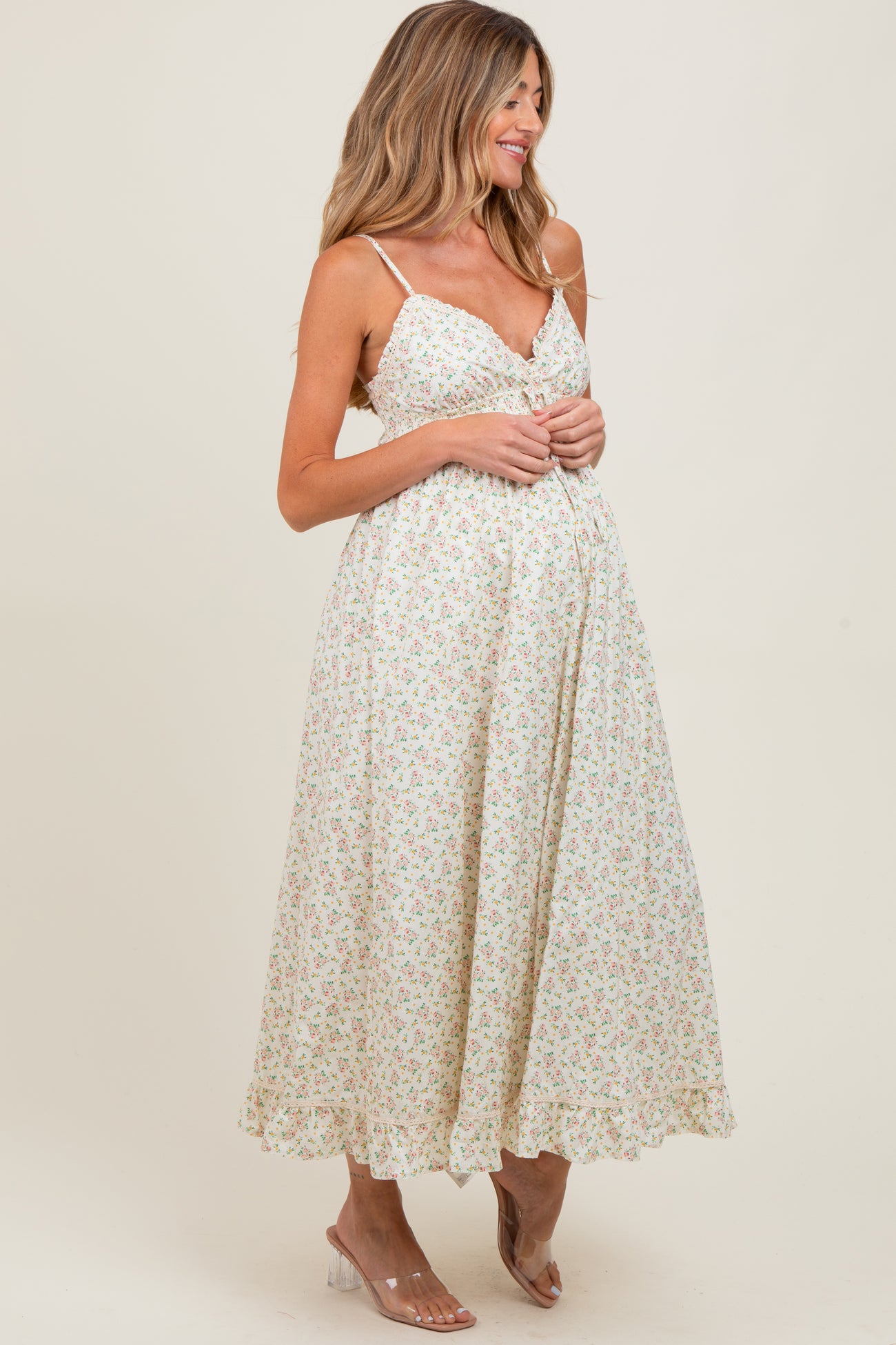 woman wearing a floral print maternity maxi dress with adjustable straps and a flowing skirt, showcasing her baby bump