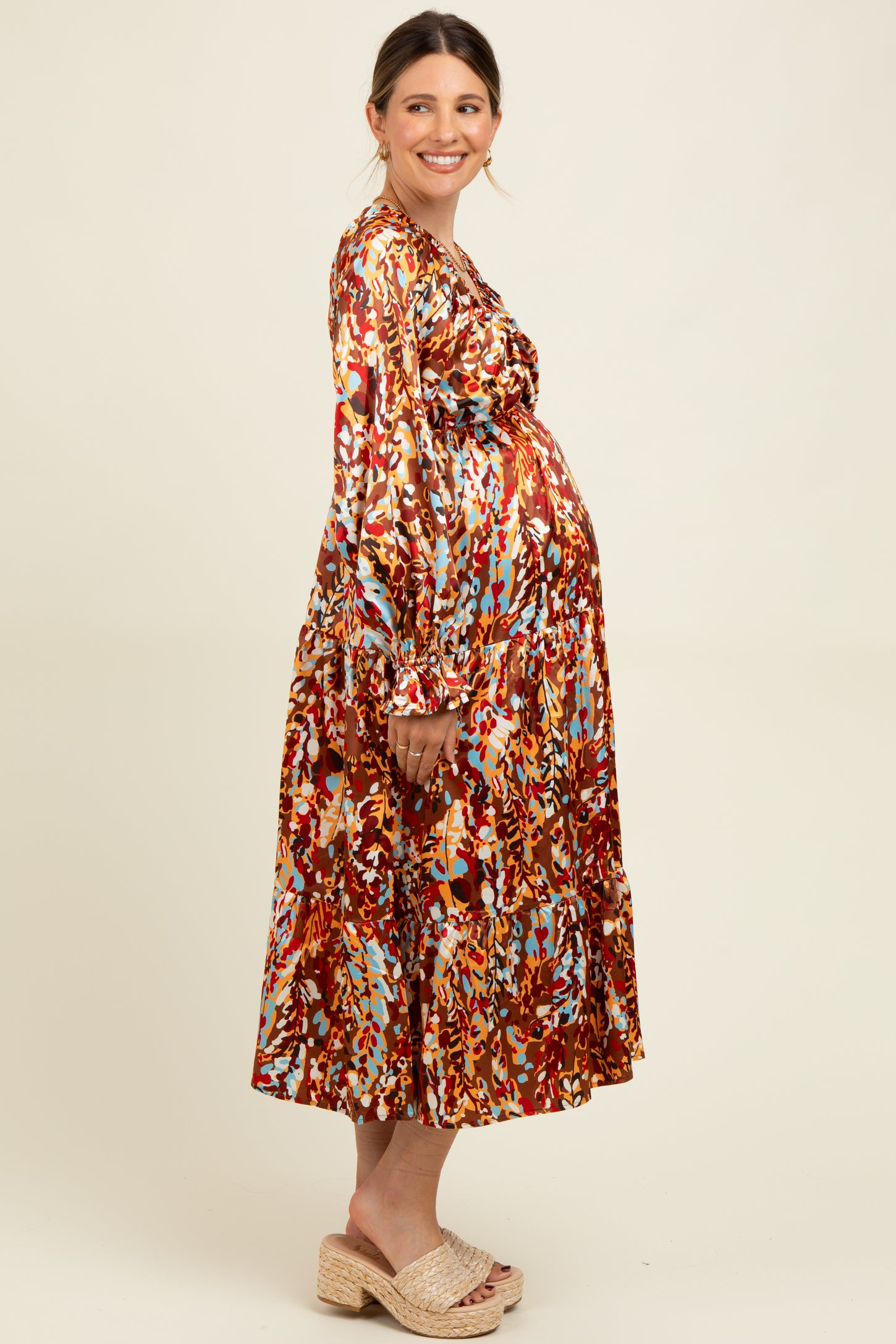 woman wearing a colorful patterned maternity dress with long sleeves and a flowy skirt, showing her baby bump