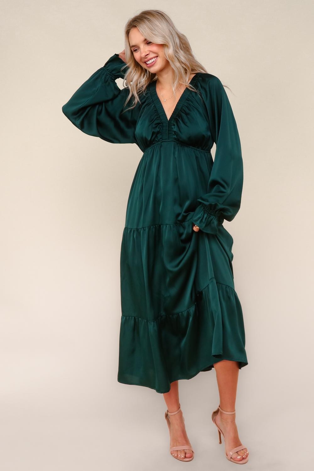 woman wearing a dark green tiered maxi dress with long sleeves and a deep v-neckline, smiling against a neutral background