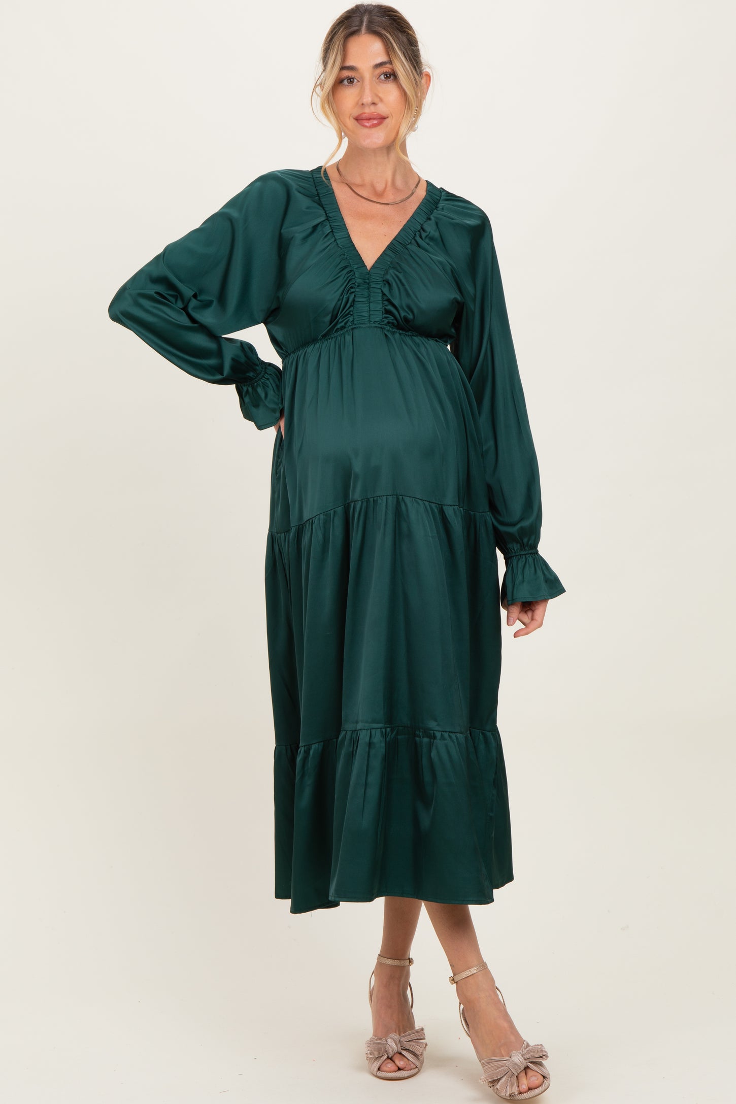 woman wearing a dark green maternity dress with a v-neck and tiered design, showcasing her baby bump