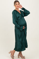 woman wearing a dark green maternity dress with a ruffled neckline and puff sleeves, showcasing her baby bump