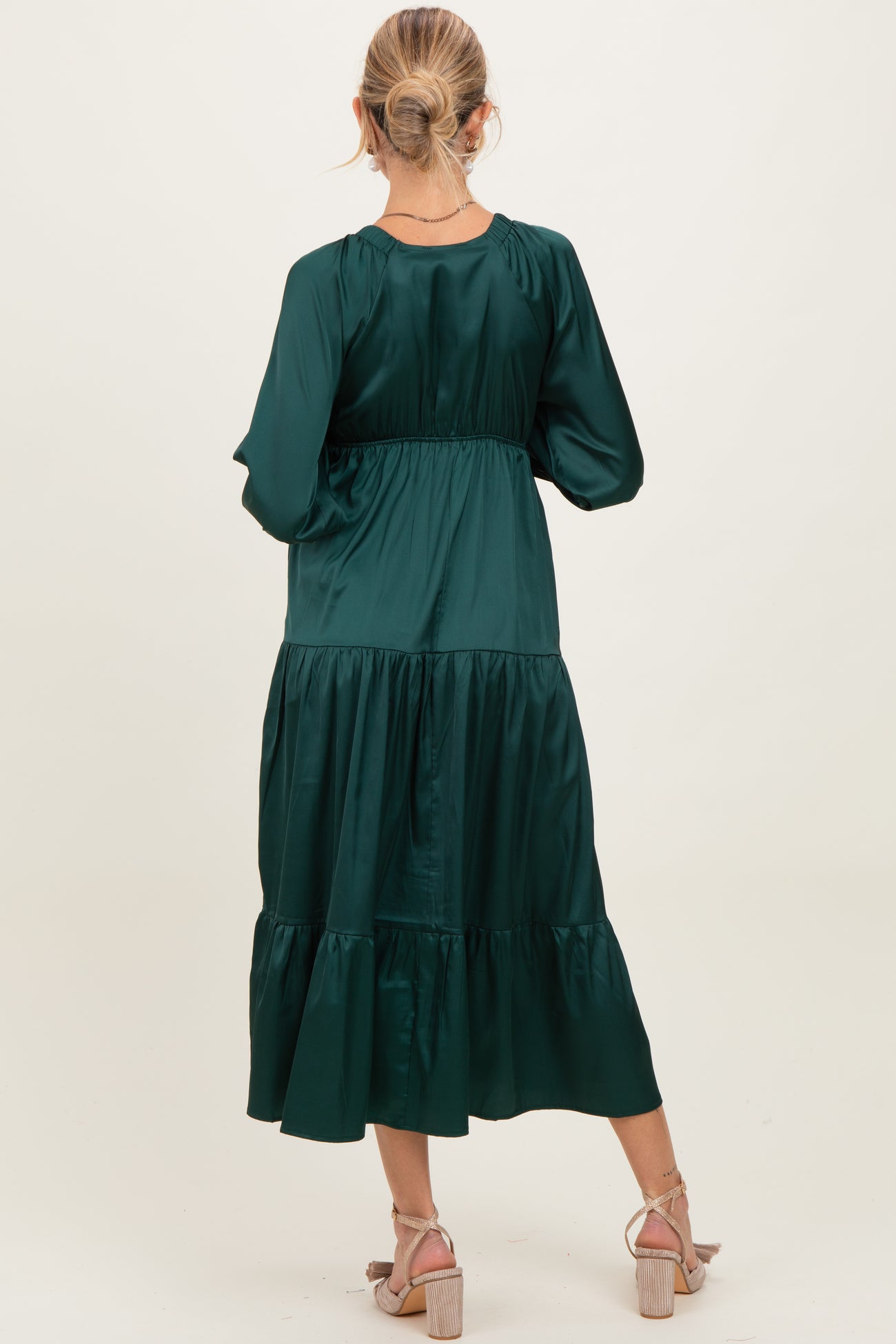 woman wearing a dark green satin maternity dress with a tiered skirt and long sleeves, showing the back view