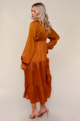 woman wearing a rust orange long sleeve maxi dress with tiered skirt and elastic waistband, standing with back facing the camera