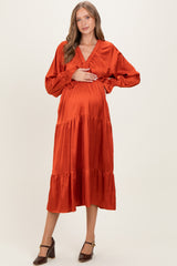 woman wearing an orange maternity midi dress with long sleeves and a tiered hem, holding her baby bump
