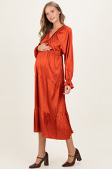 woman wearing an orange maternity maxi dress with long sleeves and a tiered skirt, holding her baby bump