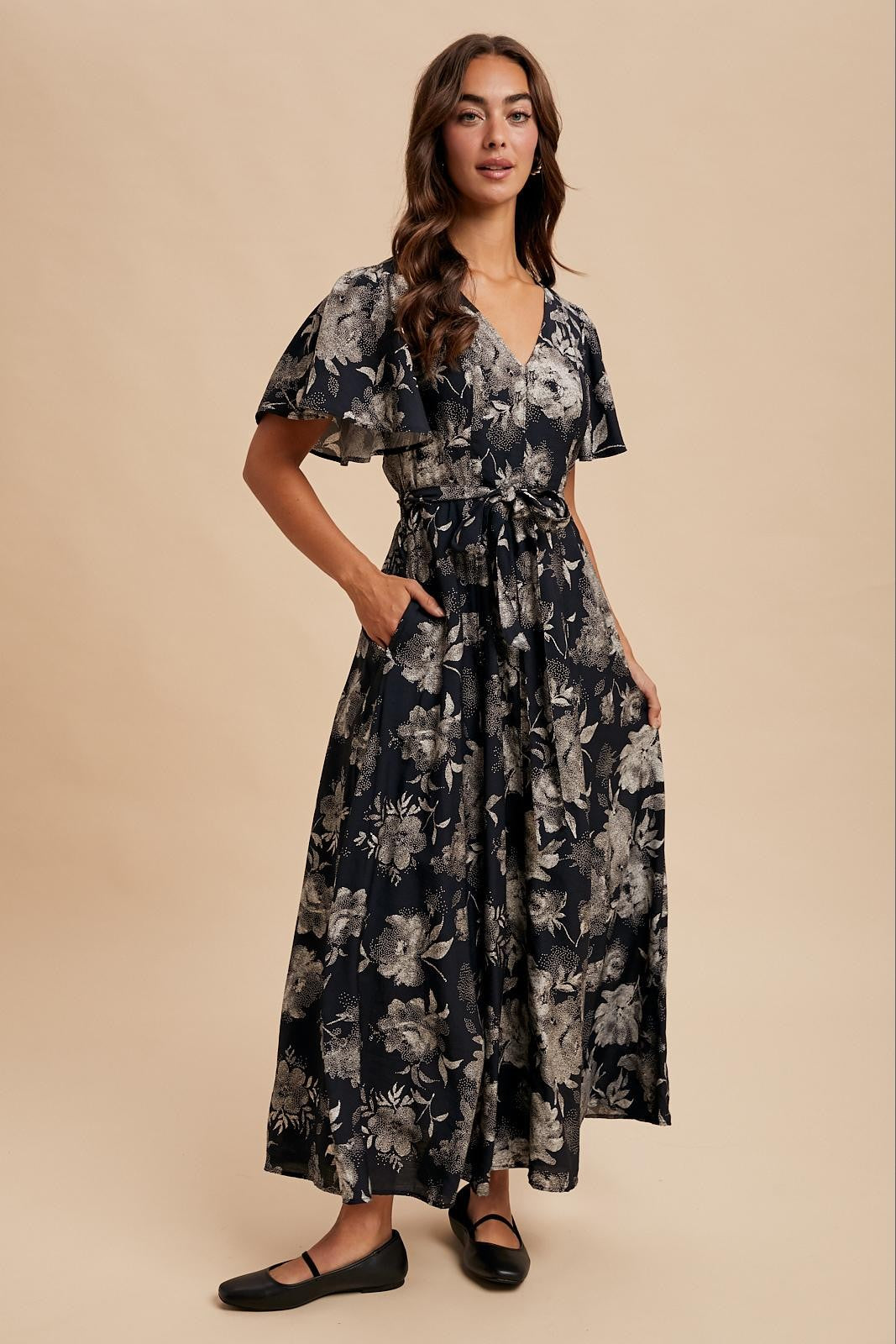 woman wearing a navy floral maxi dress with flutter sleeves and a tie waist detail, standing confidently
