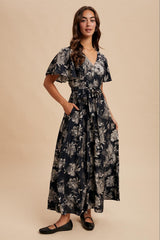 woman wearing a navy floral maxi dress with flutter sleeves and a tie waist detail, standing confidently