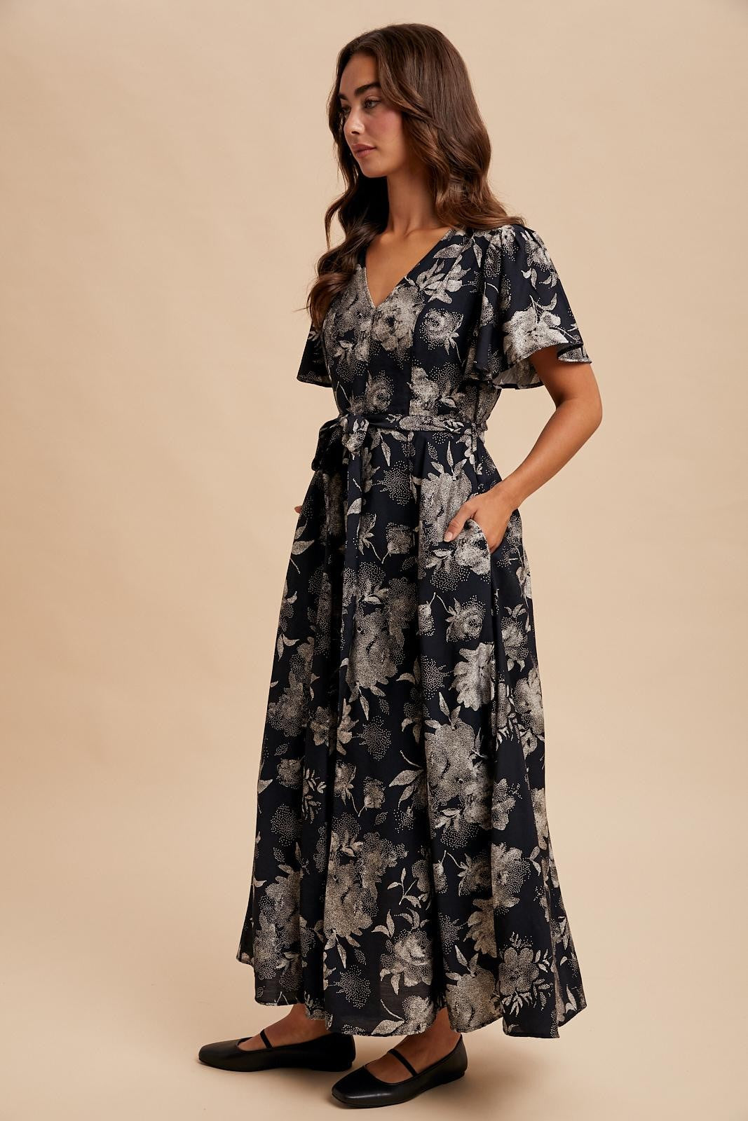 woman wearing a navy blue floral maxi dress with a v-neckline, ruffled sleeves, and pockets