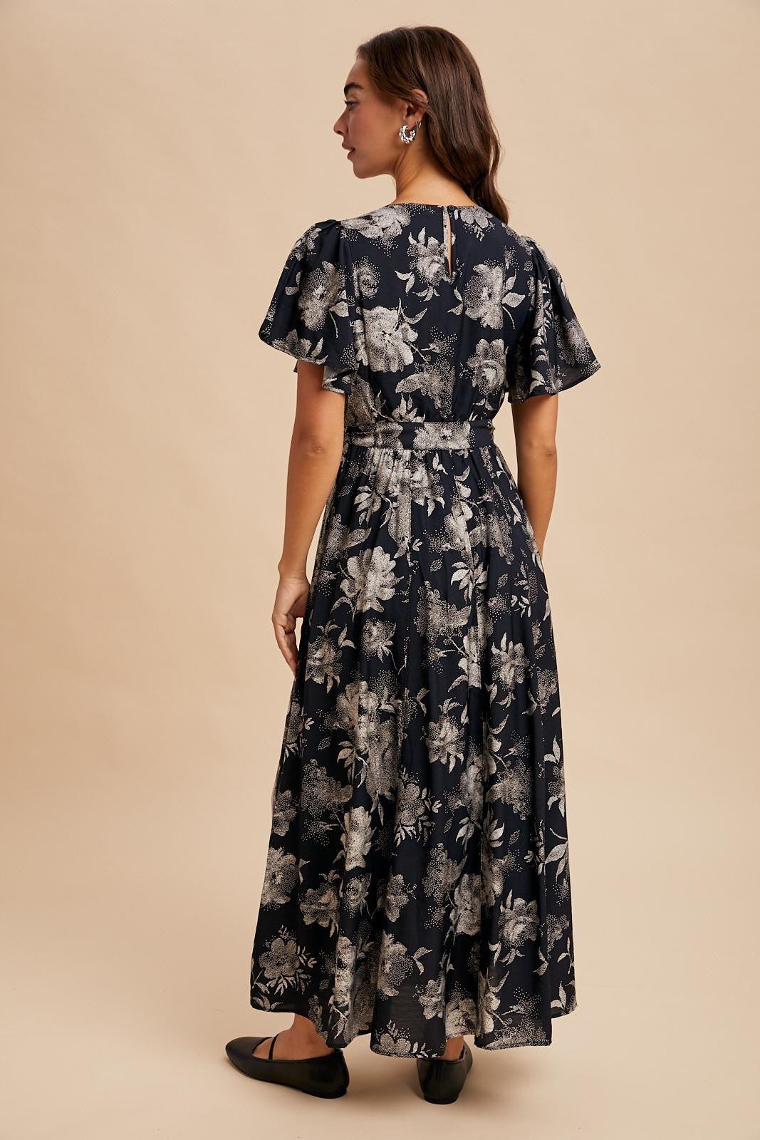 woman wearing a navy floral maxi dress with short flutter sleeves and a cinched waist, seen from the back