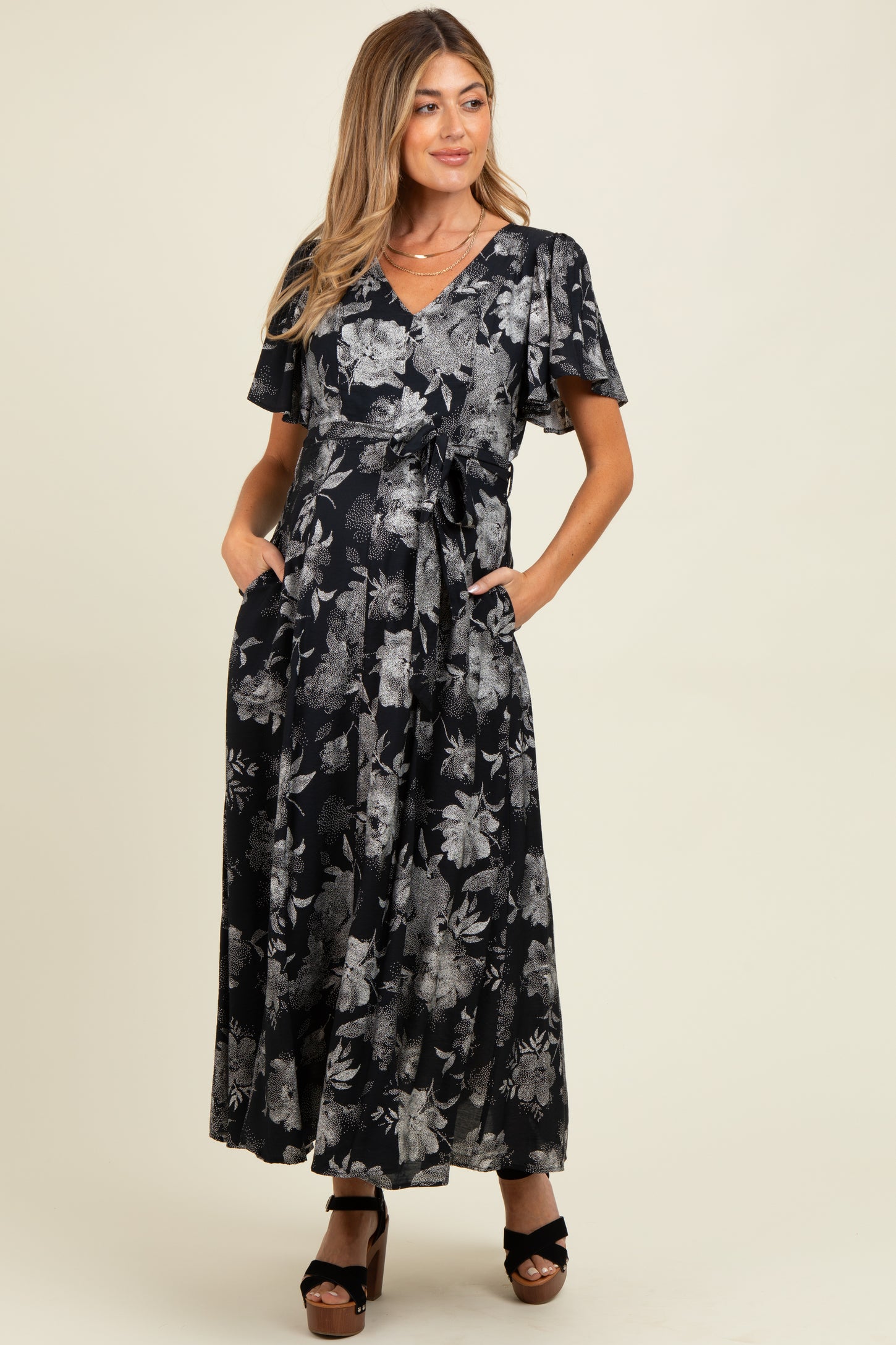 woman wearing a black floral maternity maxi dress with flutter sleeves and pockets, showcasing her baby bump