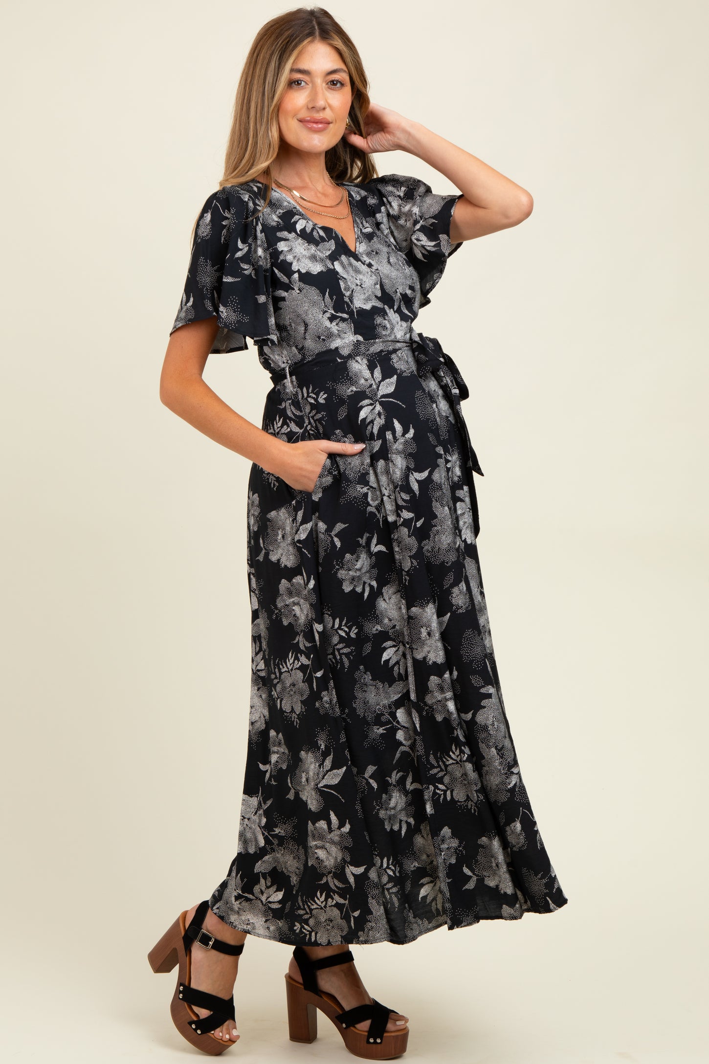 woman wearing a black floral maternity maxi dress with a tie waist and pockets, showcasing her baby bump