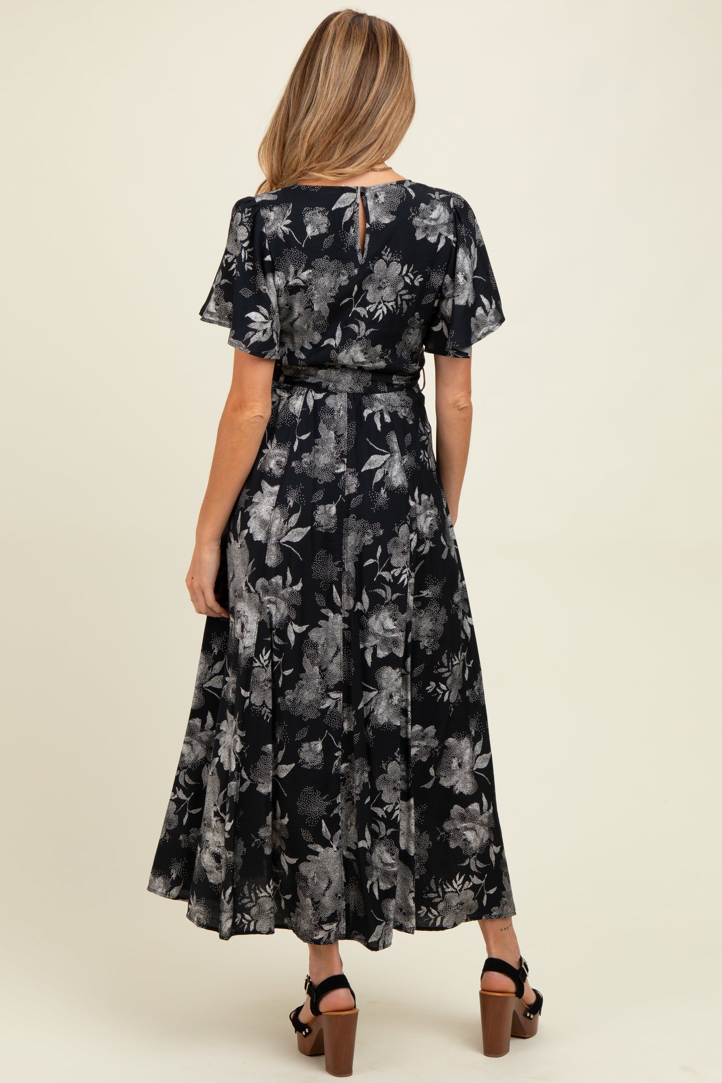 woman wearing a floral black maternity dress with short flutter sleeves and a cinched waist, showing the back view