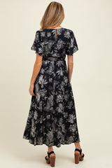 woman wearing a floral black maternity dress with short flutter sleeves and a cinched waist, showing the back view