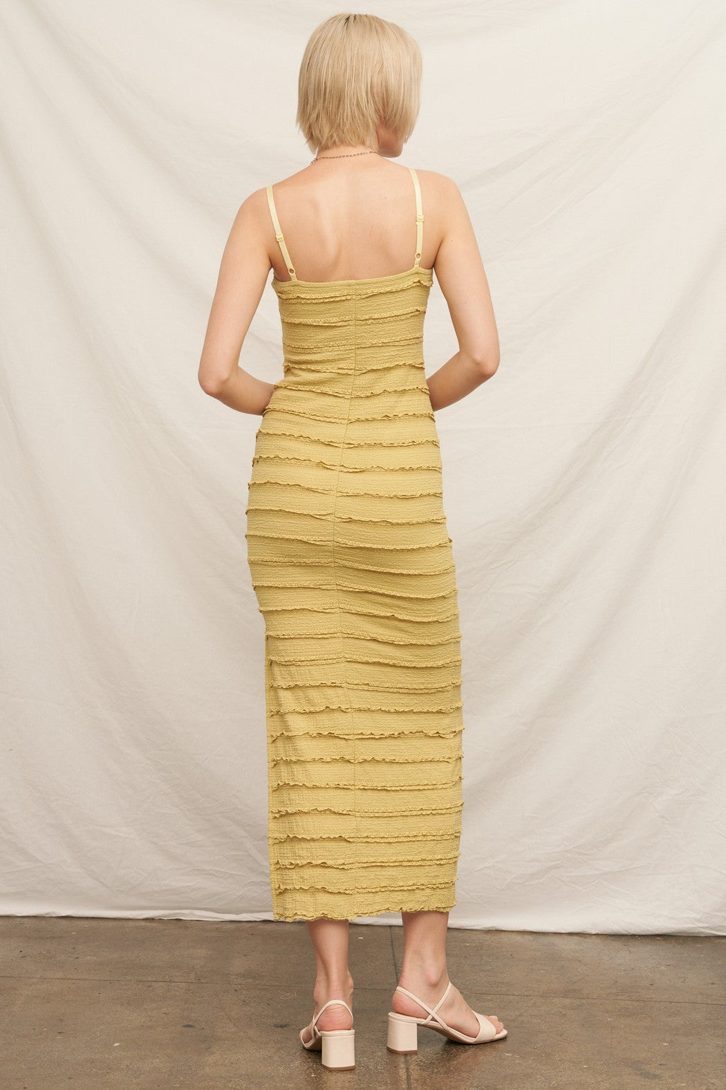 woman wearing a mustard yellow form-fitting midi dress with a textured ruffle design and thin straps