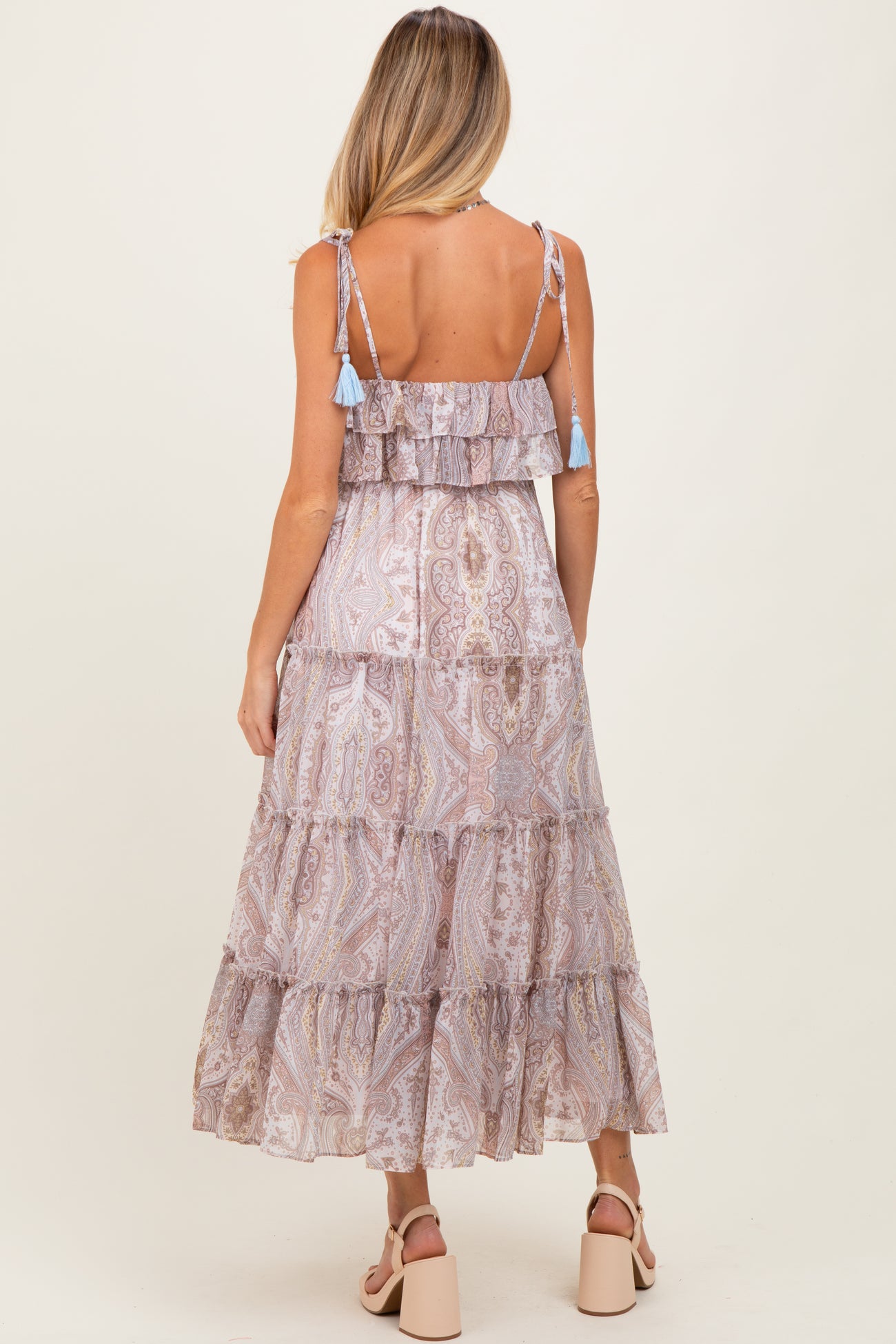 woman wearing a patterned lavender maternity maxi dress with ruffled tiers and tassel straps, showing a baby bump