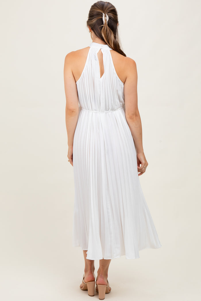 woman wearing a white pleated maternity dress with a halter neck and open back, showing a flowing skirt