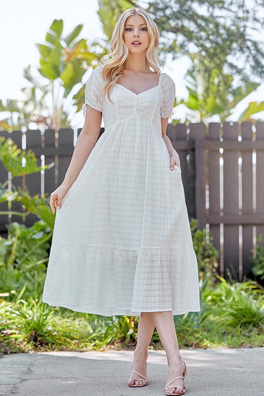 woman wearing a white midi dress with puff sleeves and a tiered skirt, standing outdoors in a sunny setting