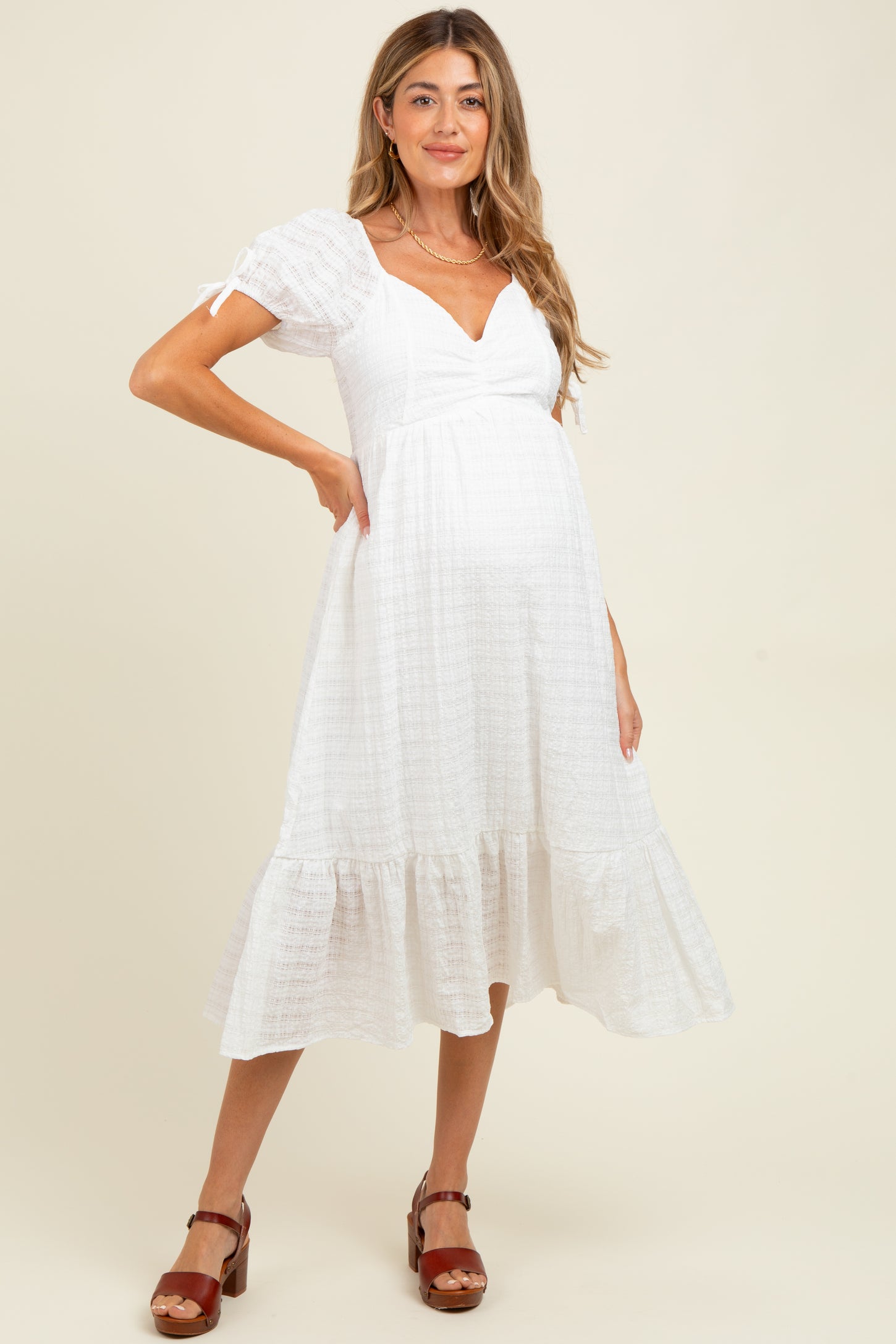 woman wearing a white maternity dress with puff sleeves and a ruffled hem, showing a baby bump