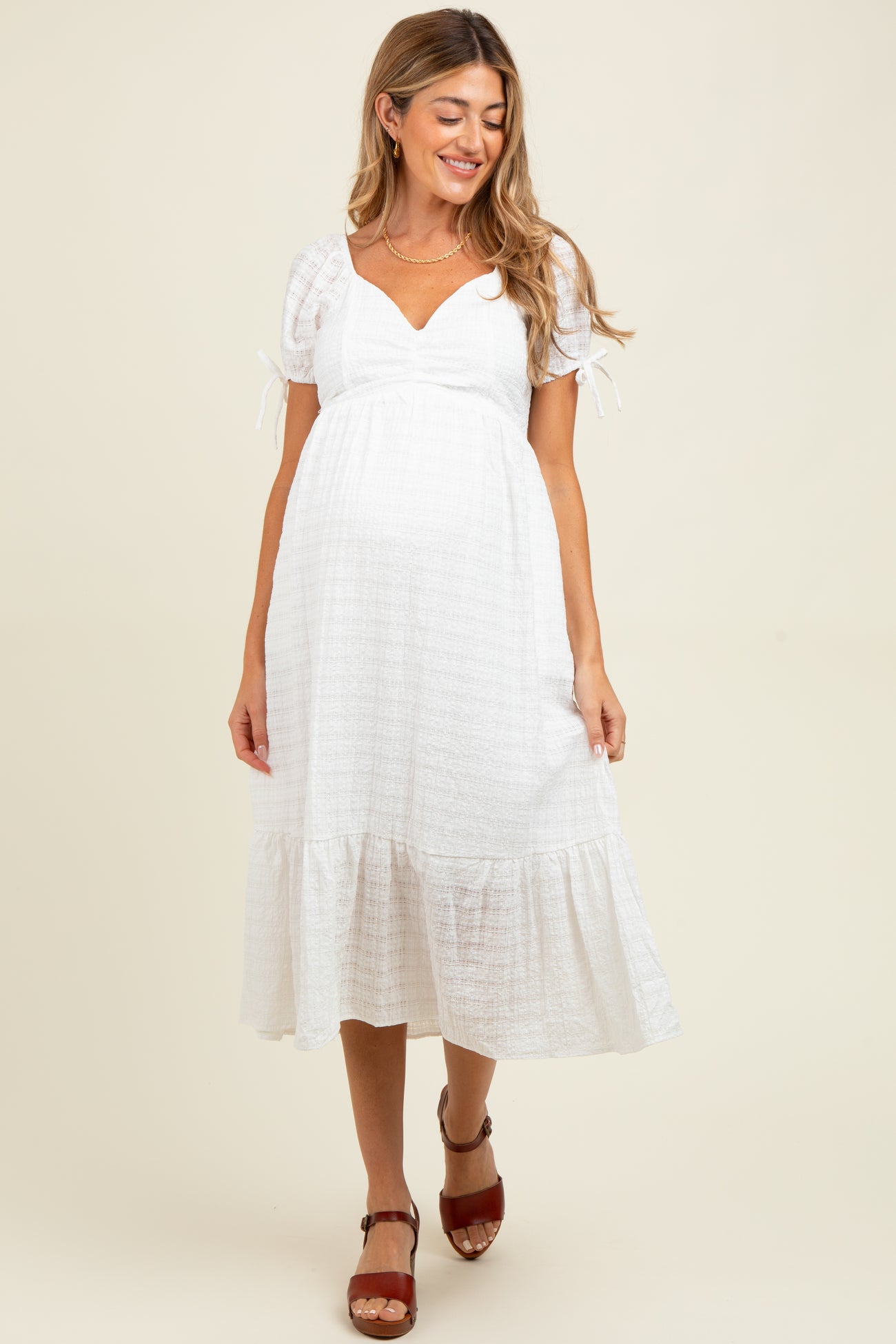 woman wearing a white maternity dress with puff sleeves and a tiered skirt, showing a baby bump