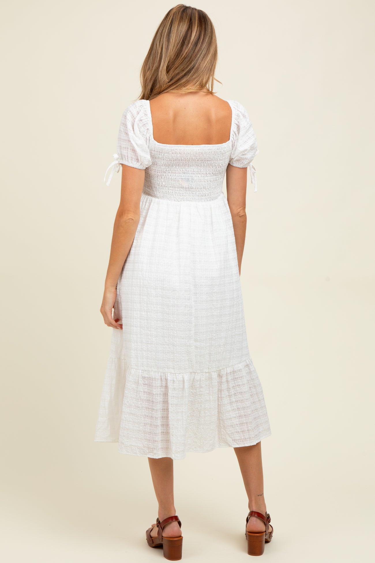 woman wearing a white smocked maternity dress with short sleeves and a tiered hem, showing a baby bump from the back