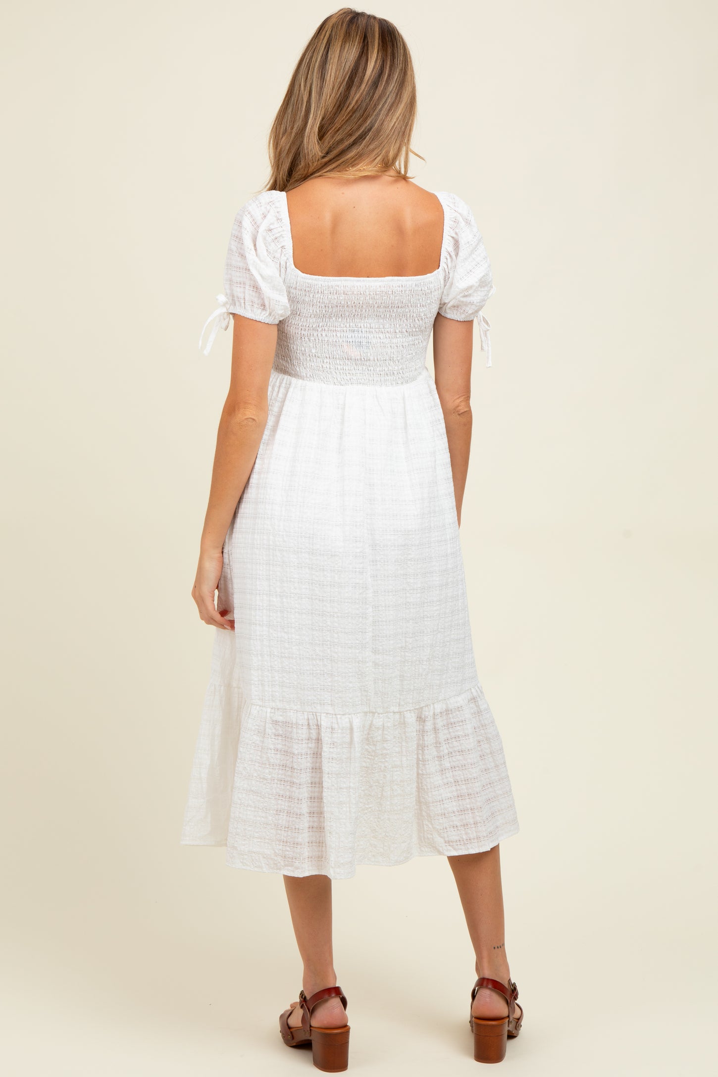 woman wearing a white smocked maternity dress with short sleeves and a tiered hem, showing a baby bump from the back