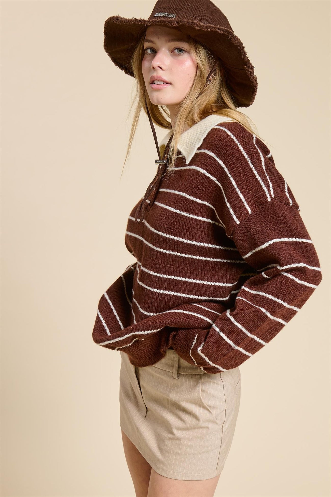 woman wearing a brown and white striped sweater with a collar and beige shorts, styled with a brown bucket hat