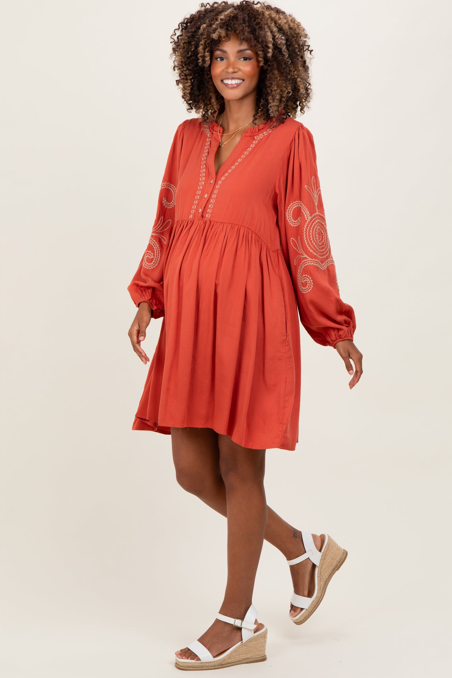woman wearing a rust-colored long sleeve maternity dress with embroidery and a visible baby bump