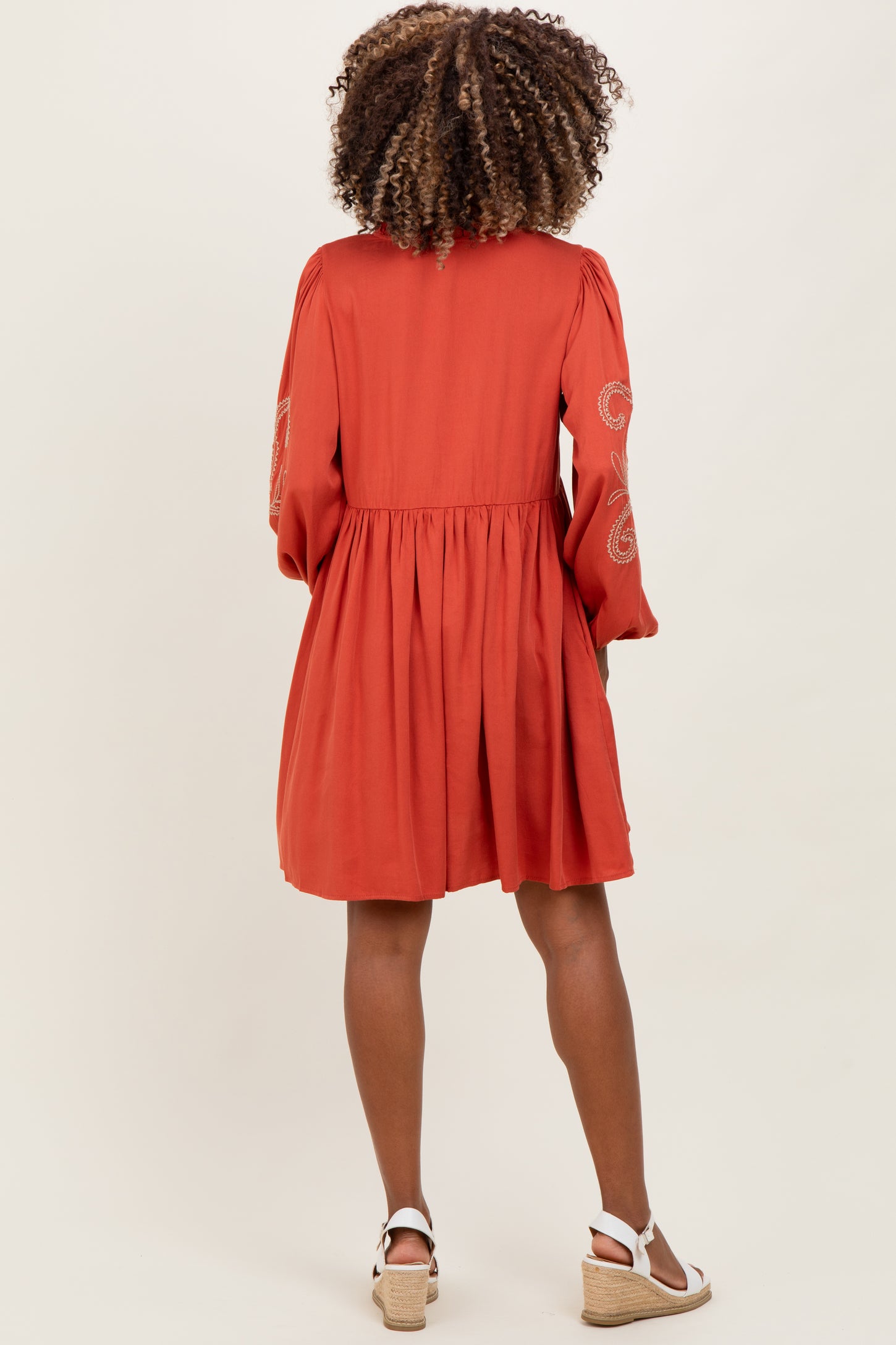 woman wearing a rust colored maternity dress with embroidered sleeves and a flared skirt from the back