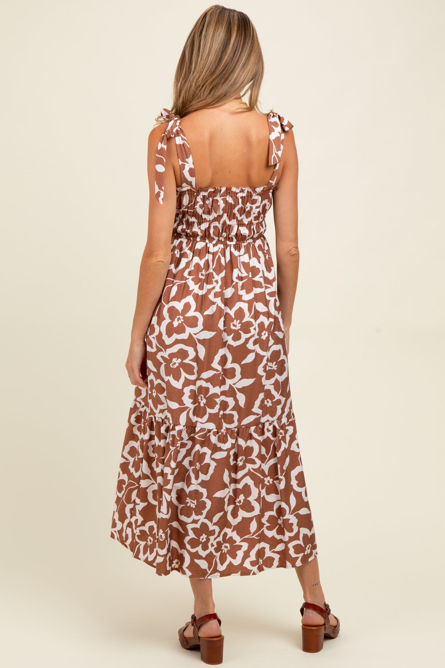 woman wearing a brown floral maternity dress with tie straps and a smocked back, showing a loose fit and tiered hem