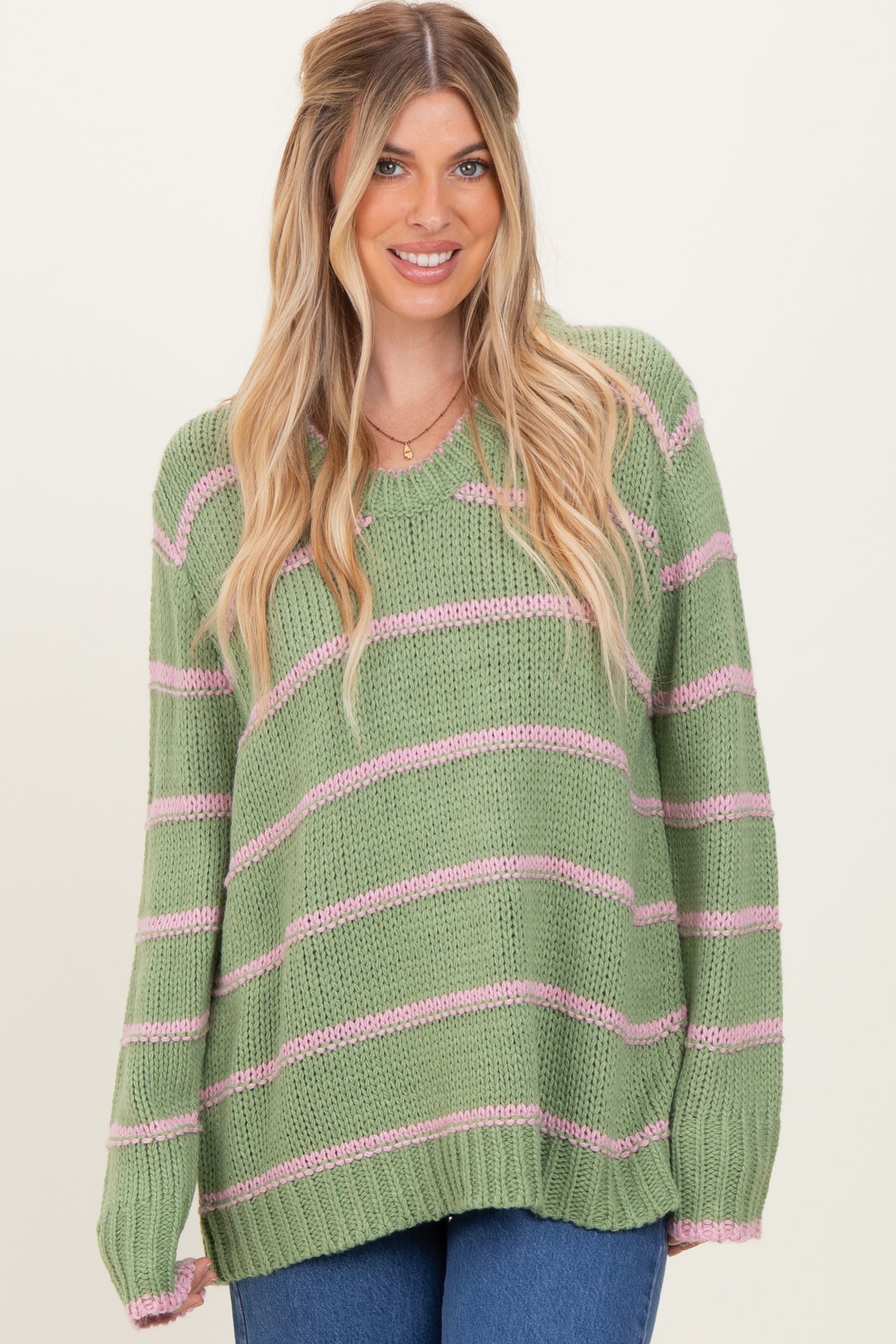 woman wearing a light green striped sweater with pink stripes and a relaxed fit, smiling at the camera