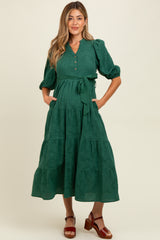 woman wearing a green maternity dress with short puff sleeves, button details, and a tie waist, showcasing her baby bump