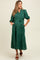 woman wearing a dark green maternity maxi dress with three-quarter sleeves, button details, and a tie belt, showing baby bump