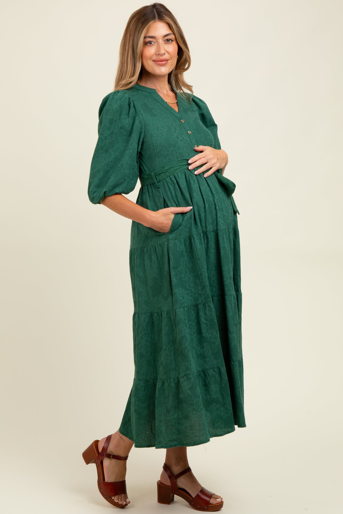 woman wearing a dark green maternity maxi dress with pockets and a tiered design, highlighting her baby bump