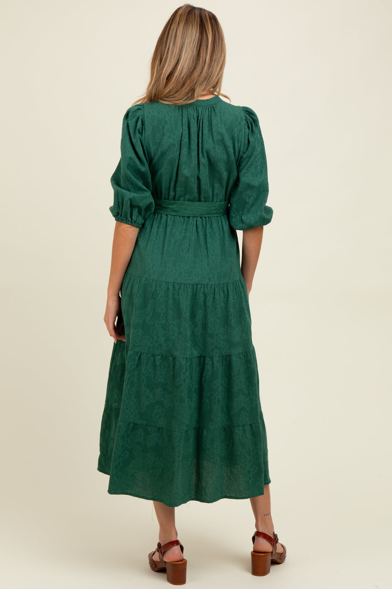 woman wearing a dark green maternity dress with puff sleeves and a tiered skirt, showing her baby bump from the back