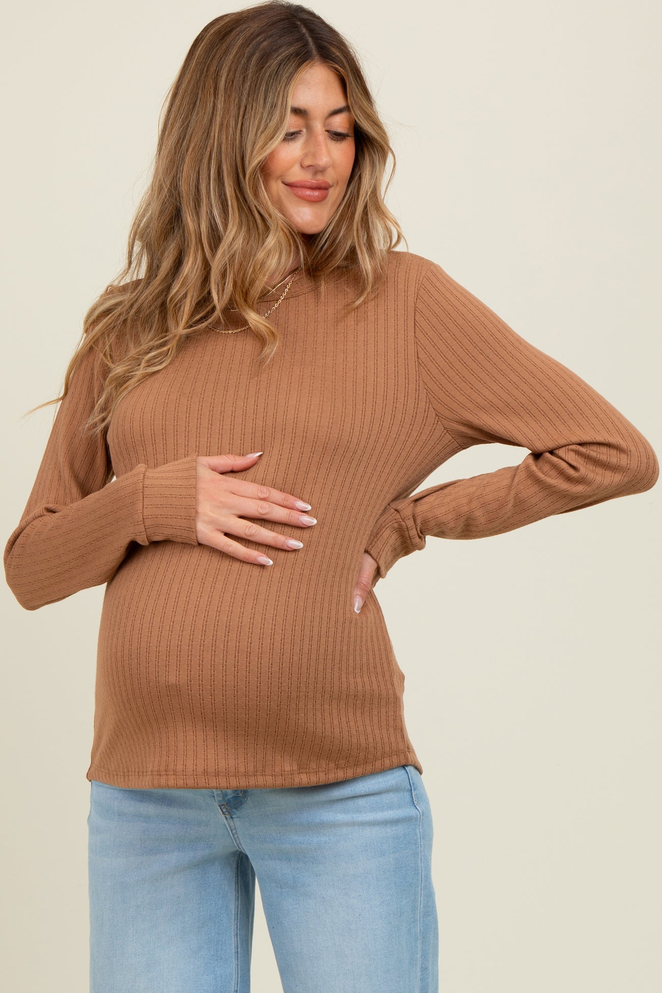 woman wearing a ribbed tan maternity top and holding her baby bump