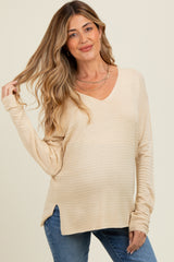 woman wearing a light beige maternity long sleeve top with a v-neck and side slits, showcasing her baby bump
