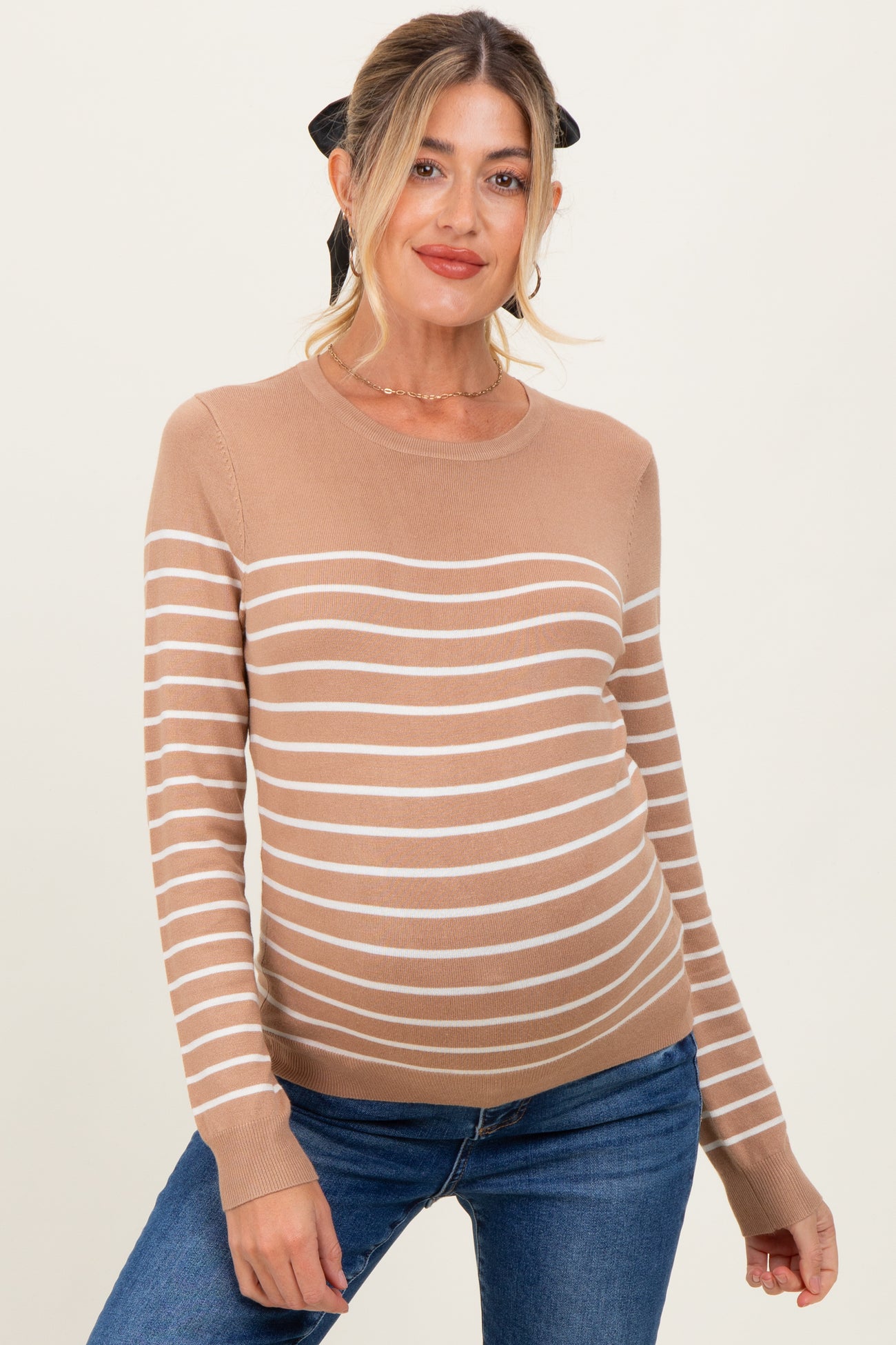 woman wearing a tan striped maternity sweater with a round neckline and long sleeves, showcasing her baby bump